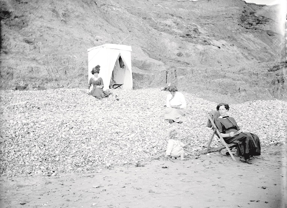Beach scene at the Isle of Wight in 1913, with Alfred’s mother in the background.  The woman with the white blouse is probably his sister Irene Barton/Lock with her daughter Alison born in 1911.  The other sister in the deckchair might be Ethel Grace.  Glass plate negative.